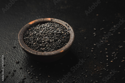 Black sesame seeds in small bowl on black background
