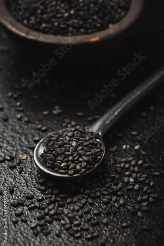Black sesame seeds in small bowl on black background