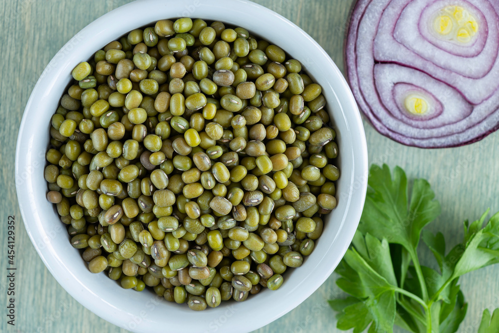 top view on beans of mung sin white plate with onion and parsley. close up mung on a green wooden background. Flat lay. top view on beans of mung sin white plate with onion and parsley. close up mung on a green wooden background. Flat lay.