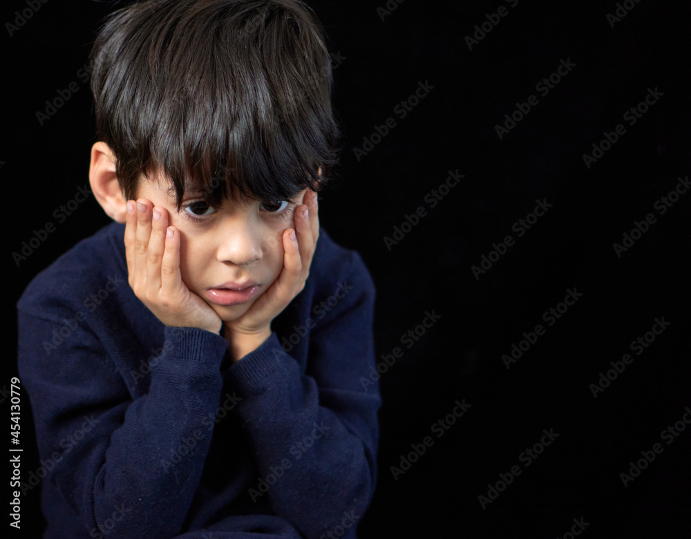 closeup portrait of latino kid with a blank stare worried and pensive resting his face on his hands. black background and copy closeup portrait of latino kid with a blank stare worried and pensive resting his face on his hands. black background and copy