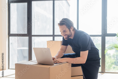happy mover typing on laptop near cardboard boxes