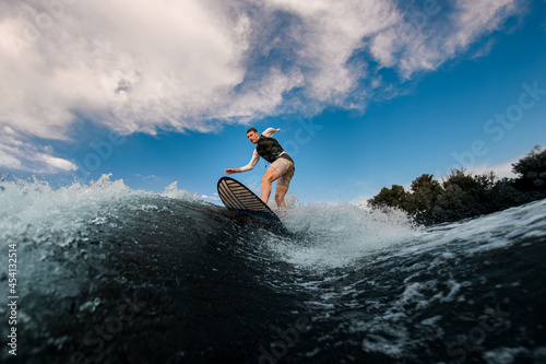 athletic one-armed man standing on surfboard and rides the wave. Wakesurfing on the river