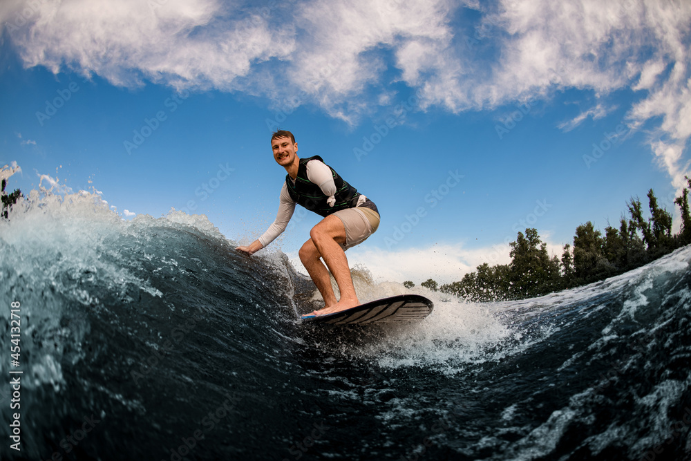 armless man wakesurfing on the board down the wave against the background of sky