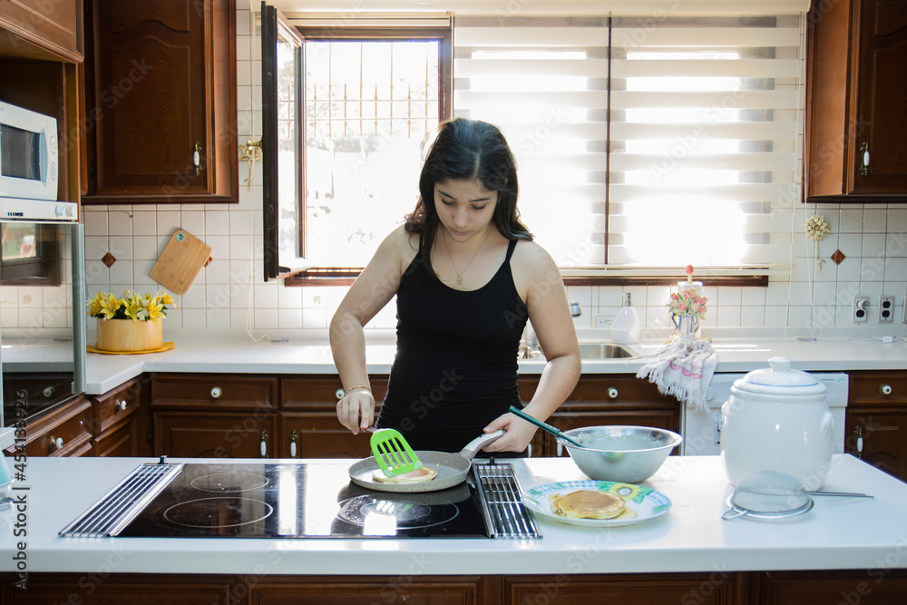 young girl is cooking pancakes for breakfast in the kitchen of her home. Selective Focus Girl