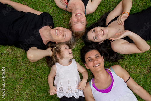 young women and girls from the same family, lying on the grass, smiling together. © Yasin