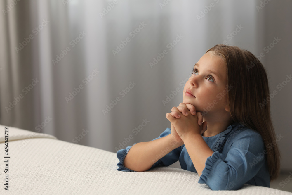 Cute little girl with hands clasped together saying bedtime prayer in bedroom. Space for text Cute little girl with hands clasped together saying bedtime prayer in bedroom. Space for text