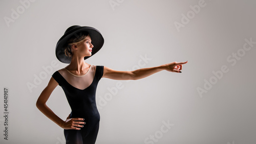 Romantic portrait of beautiful young girl on light background in an elegant hat pointing to the right