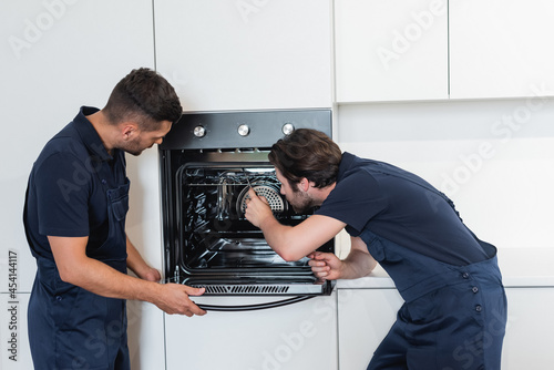 workmen in overalls repairing electric oven in kitchen