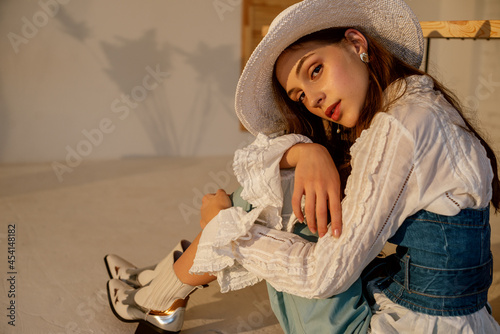 Fashionable woman wearing trendy  white hat, vintage shirt, denim corset, cowboy boots. Model posing in studio. Copy, empty space for text