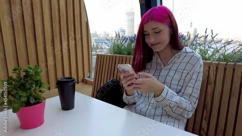  Happy red-haired student girl laughs heartily chatting on a smartphone in social networks sitting in cafe. High quality 4k footage photo