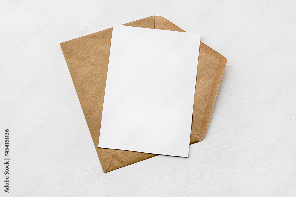 An envelope made of kraft paper and a white blank card on a white table. Blank or empty postcard. - obrazy, fototapety, plakaty 