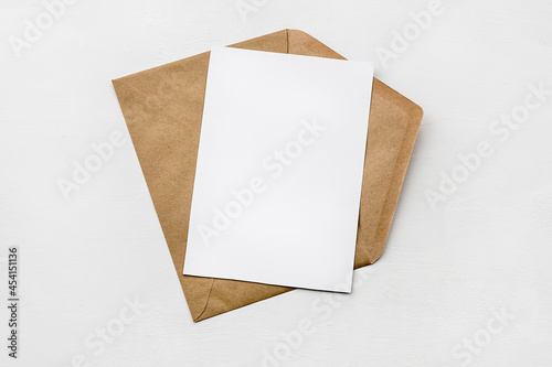 An envelope made of kraft paper and a white blank card on a white table. Blank or empty postcard.