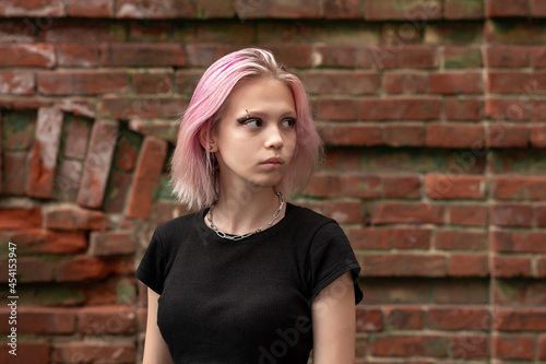 portrait of a teenage girl with pink hair on a brick wall background © Evgeny