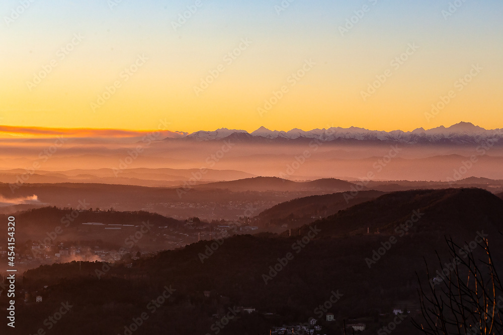 View of the misty and fog surrounding the mountains of the Italian Alps at winter sunset. Layers of mountains. Nature tourism. View of the misty and fog surrounding the mountains of the Italian Alps at winter sunset. Layers of mountains. Nature tourism.