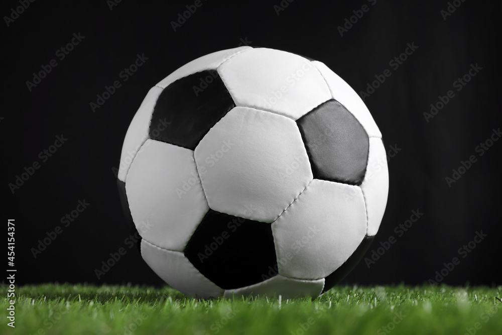 Fototapeta premium Football ball on green grass against black background