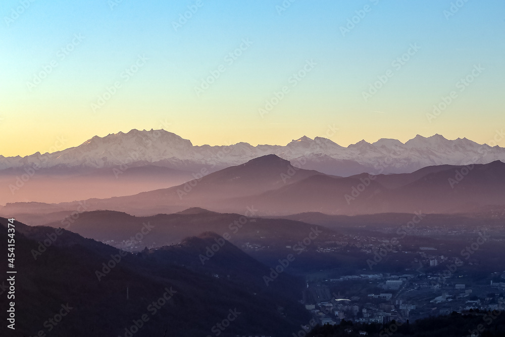 View of the misty and fog surrounding the mountains of the Italian Alps at winter sunset. Layers of mountains. Nature tourism.