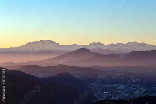 View of the misty and fog surrounding the mountains of the Italian Alps at winter sunset. Layers of mountains. Nature tourism. © Fernando Calmon
