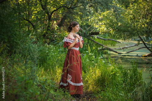 Bild auf Leinwand Sad young woman in a 19th century dress by the river with a book in her hands