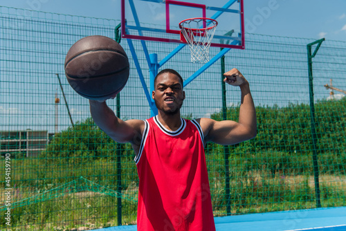 African american sportsman showing muscles and holding basketball ball on playground
