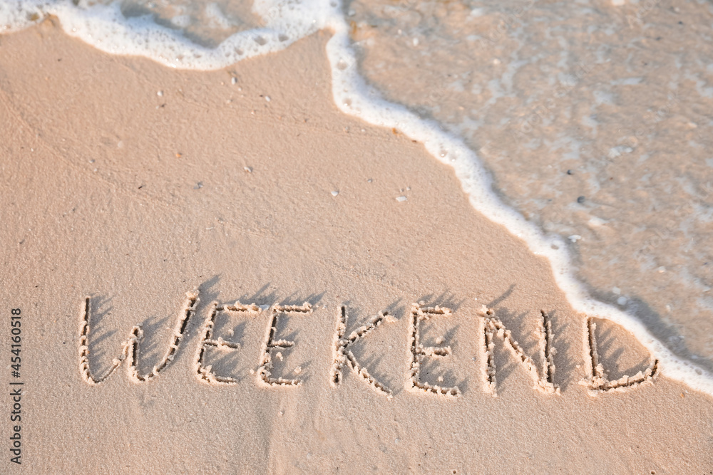Fototapeta premium Word Weekend written on sand at beach, above view