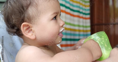 Portrait of a little boy who sits on a child's chair. Happy child drinks milk, kefir or dairy products from a cup. Correct and natural nutrition for children