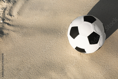 Soccer ball on sand, above view with space for text. Football equipment
