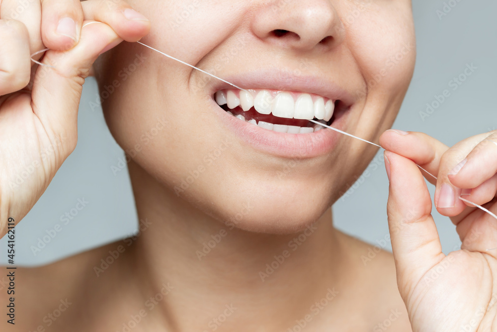 Obraz premium A cropped shot of a young beautiful caucasian woman flossing her teeth isolated on a gray background. Close-up. Oral hygiene, dental health care, morning and evening routine. Dentistry concept