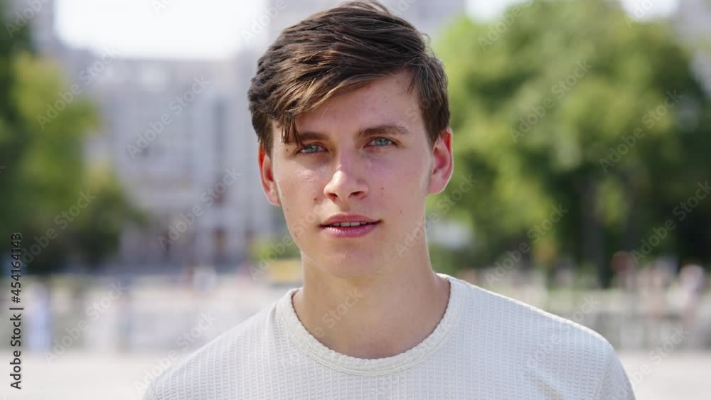 Attractive man with moles on face wearing t-shirt looking at camera, sunshine on his face, blurred background. Closeup portrait of male model in city on summer day Attractive man with moles on face wearing t-shirt looking at camera, sunshine on his face, blurred background. Closeup portrait of male model in city on summer day