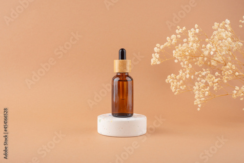 Amber glass dropper bottle with bamboo lid on white podium for product presentation on beige background with dry plants. Skincare products ,natural cosmetic. Beauty concept for face and body care