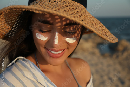 Happy young woman with sun protection cream on face at beach