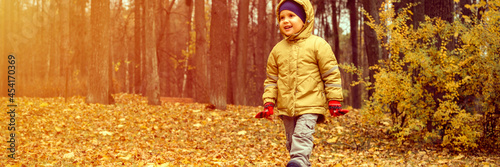 a little four year old kid happy smiling boy walks in an autumn forest or park. banner. flare