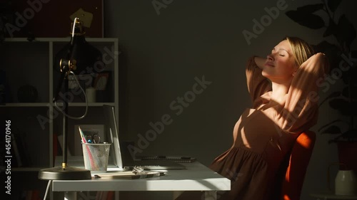 Young smiling woman resting at workplace. Happy business woman lying on chair and relaxing. Remote workplace, home office concept. Executive female manager sitting in sun rays.  photo