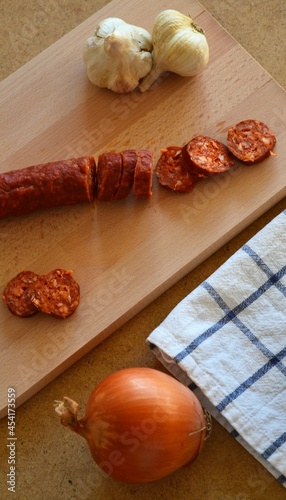 Chorizo ​​cut on a wooden board surrounded by onion and garlic photo