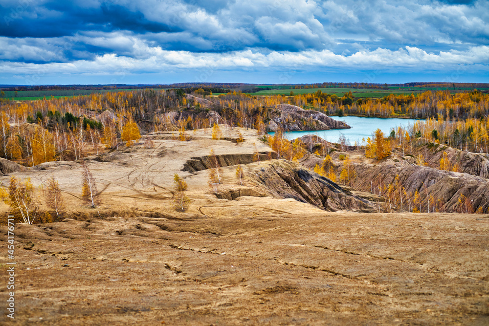 Trees with autumn yellow foliage on sand dunes and a blue lake.