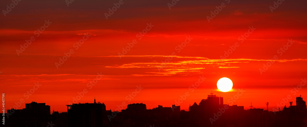 Black outline of the night city against the background of a bright red sunrise in the early morning.