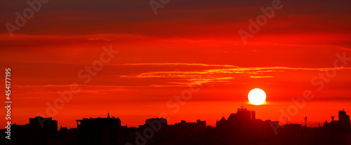 Obraz na płótnie Black outline of the night city against the background of a bright red sunrise in the early morning. w salonie