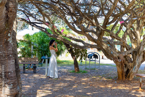 A brunette woman wearing a mask photographing a garden in a square. Public park.