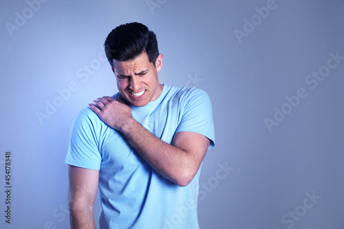 Man suffering from shoulder pain on color background