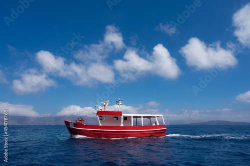 Small red fishing boat in blue sea water. Silhouettes of islands on background.