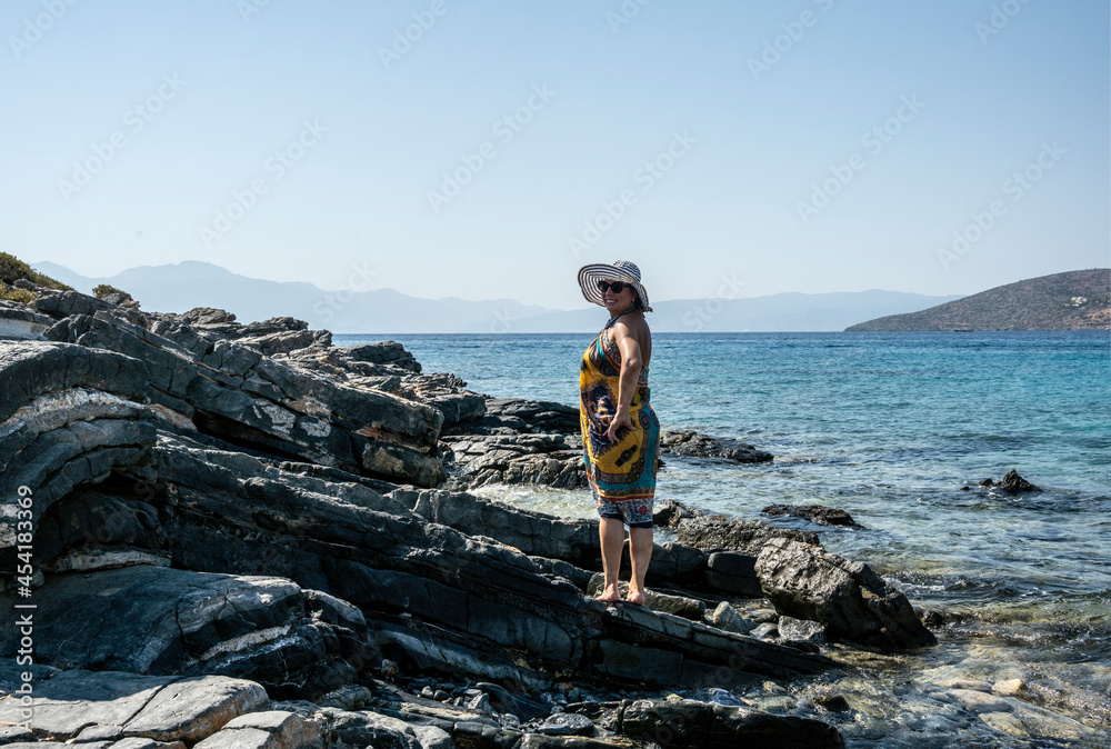 woman in white hat posing on stones against the background of the sea 