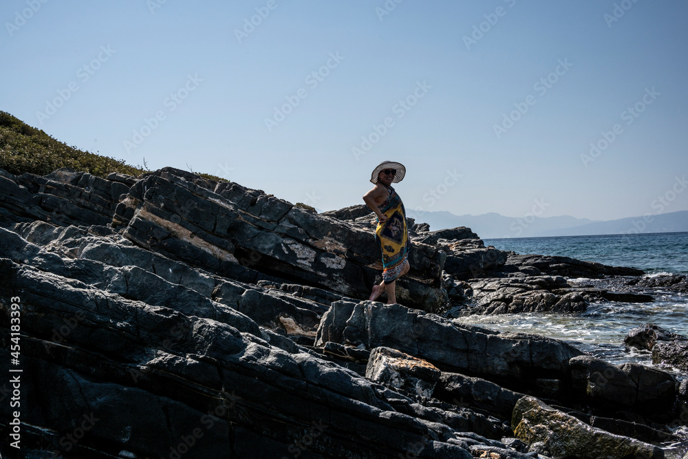 woman in white hat posing on stones against the background of the sea woman in white hat posing on stones against the background of the sea
