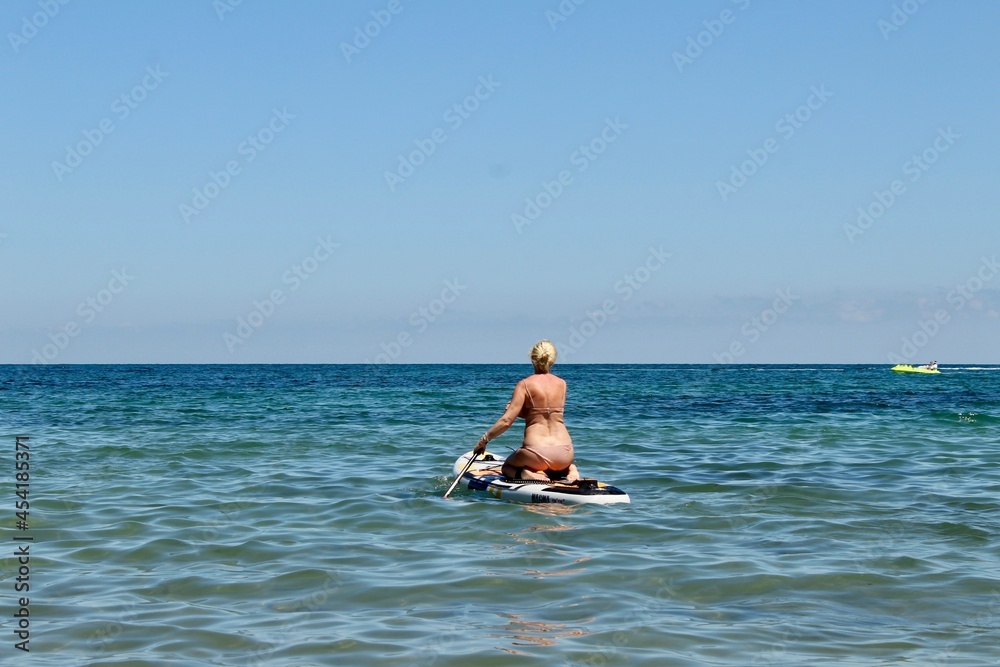 SUP Woman in beige bikini on stand up paddle board. Standup paddleboarding in the blue sea