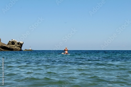 SUP Woman in beige bikini on stand up paddle board. Standup paddleboarding in the blue sea
