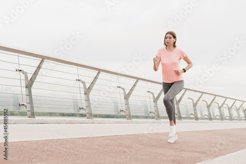 Keeping body fit slim in perfect shape. Dieting concept. Young female runner jogger running on city bridge in fitness outfit. Healthy active lifestyle © InsideCreativeHouse