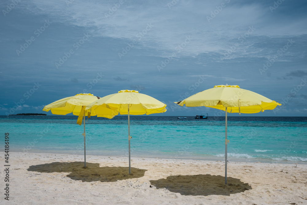 Yellow umbrellas on the white sand beach of the Maldives. Travel and recreation.