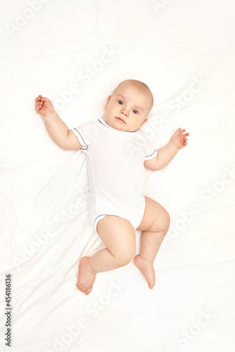 Cute small boy at house. Childhood concept. Light background. Smiling child. Happy emotion. Copyspace. Stay home. Onesie mockup. White clothes. Lying at bed