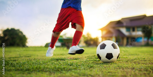 Boy kicking a ball while playing street soccer football on the green grass field for exercise. Outdoor sport activity for children and kids concept photo with copy space. © nateejindakum