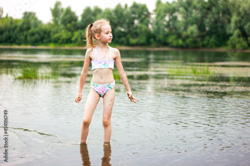 a little girl in a swimsuit stands in the river and looks into the distance, summer vacation with family