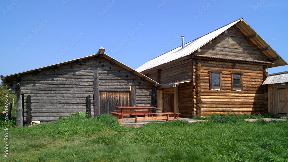 Wooden house made of logs, green grass, blue sky. House in the village Wooden house made of logs, green grass, blue sky. House in the village