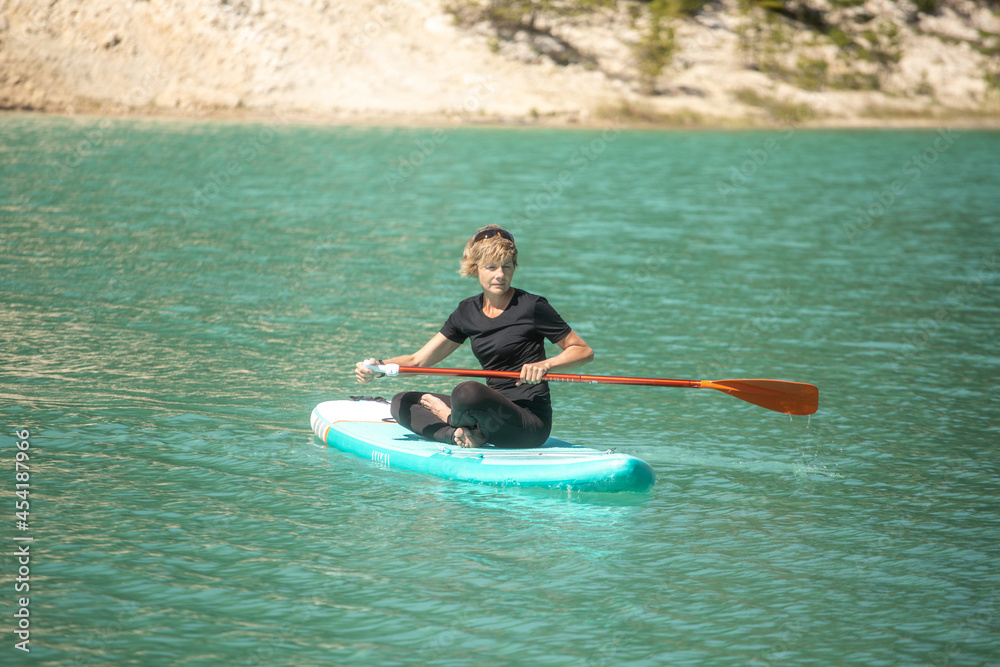 SUP concept surfboard - cute young woman is paddling on a beautiful lake with turquoise water SUP concept surfboard - cute young woman is paddling on a beautiful lake with turquoise water